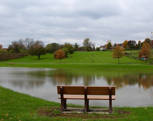 A view of the lake and the grass field of the park from behind the bench.