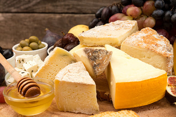 Food composition with blocks of moldy cheese, pickled plums, honey, grape bunch, olives, figs, pear, crackers on wooden background.