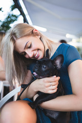 Beautiful young woman sitting in cafe with her adorable French bulldog puppy. People with dogs theme.