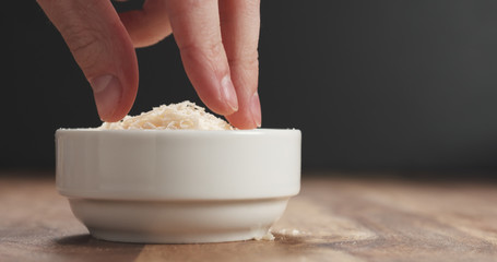 pinching grated aged parmesan from white bowl on wood table