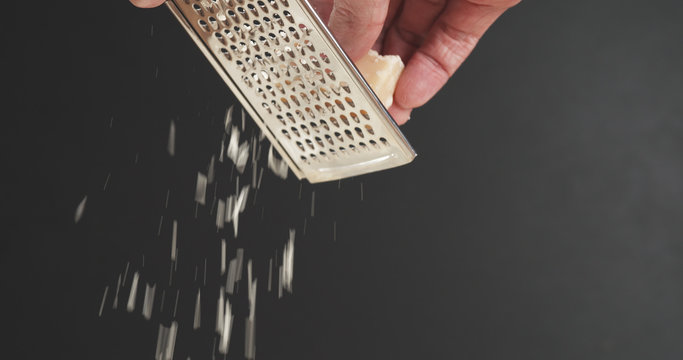 Closeup Of Grating Aged Parmesan Over Dark Background