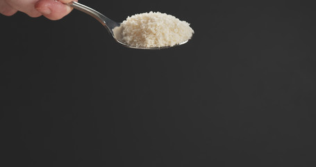 closeup of grated aged parmesan in spoon over dark background