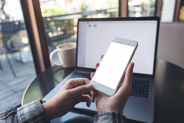 Mockup image of business woman holding mobile phone with blank white screen while using laptop on...