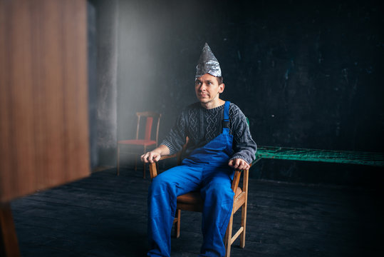 Man in tinfoil hat sits in chair, paranoia concept