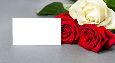 Three roses with blank white card on a  grey background.