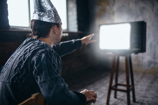Man in aluminum foil helmet reaches out to the TV