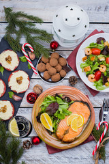 Christmas or New Year Family Dinner Setting Table Concept with Holiday Decoration. Delicious Roast Steak Salmon, Salade, Appetizers and Dessert on white wooden Background. Top view