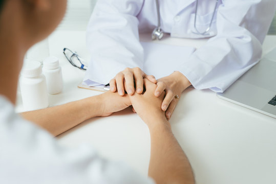Friendly female doctor hands holding patient hand sitting at the desk