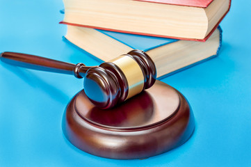 Judge's wooden gavel and stack of books on blue background.