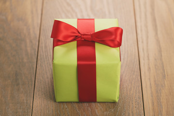 green paper gift box with red ribbon bow on oak table