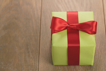 green paper gift box with red ribbon bow on oak table