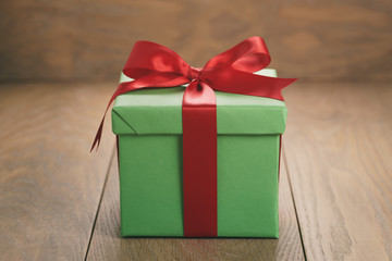 green paper gift box with red ribbon bow on oak table