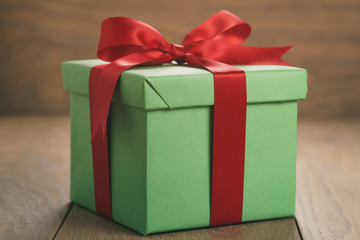 green paper gift box with red ribbon bow on oak table