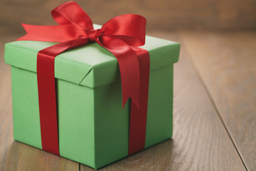 green paper gift box with red ribbon bow on oak table