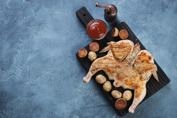 Fototapeta na wymiar Grilled tapaka chicken and cherry potato. High angle view on a blue stone background, horizontal shot with copyspace