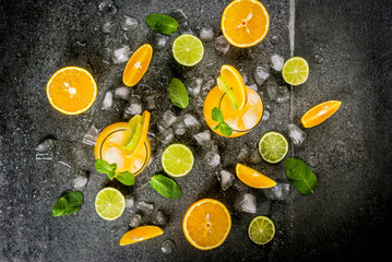 Fototapeta na wymiar Vitamin summer refreshing drinks. Citrus punch with oranges and lime, with mint sprigs, chilled with ice. On black stone table, with ingredients, copy space top view