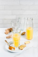 Indian cuisine recipes. Healthy food, detox water. Traditional Indian refreshing drink from turmeric and ginger, in glasses, bottles, on a white marble table. Copy space