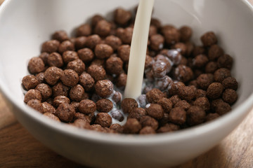 pour milk onto chocolate cereal balls in white bowl for breakfast