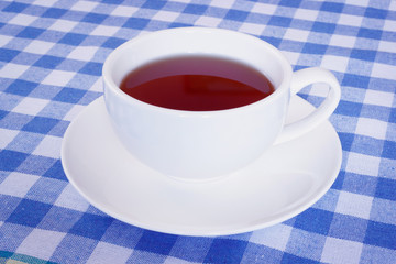 White cup of black tea on blue patchwork tablecloth