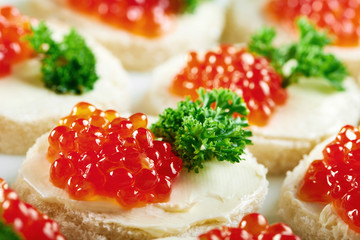 Cropped close up of red caviar on buttered bread decorated with greens delicious appetizer restaurant menu traditional seafood gourmet canapes concept.