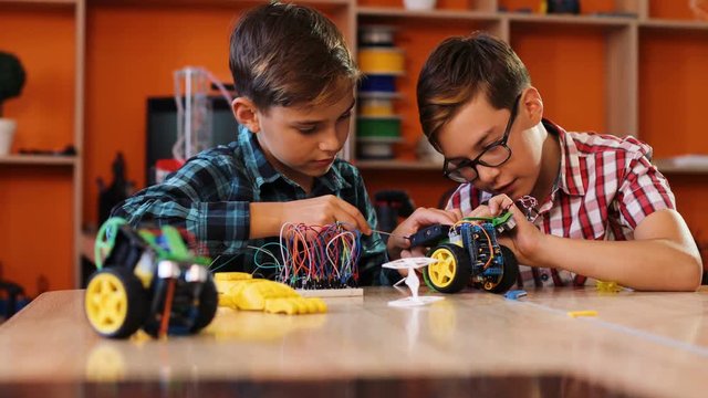 Close up of two boys managing to assemble robots with screwdrivers on the table in the modern comfortable playing classroom. Boys giving five to each other. Portrait