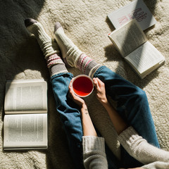Feet in woollen socks with book and cap of tea. Woman relaxes with a cup of hot drink and warming up her feet in woollen socks. - 181345257