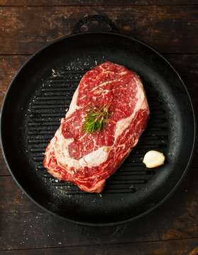 Raw fresh ribeye steak with salt, seasonings, and rosemary in a frying pan