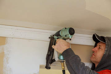 Carpenter brad using nail gun to Crown Moulding trim, warning label that all power tools