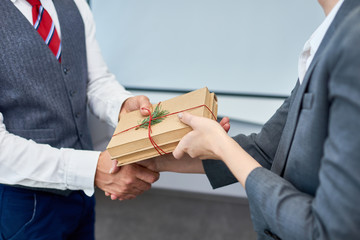 Close up view of unrecognizable businessman shaking hands with female colleague presenting her gift...