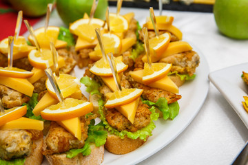 One plate with snacks on a buffet table. Selection of tasty bruschetta or canapes on toasted baguette and quark cheese topped with fried meat or fish, orange and green salad. restaurant feed.