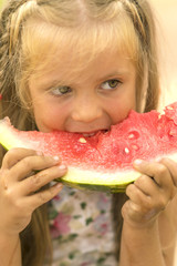 Little dirty blond girl eating a slice of red watermelon on blurred background