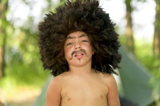 Little laughing boy in a black caucasian fur hat with painted mustache, eyebrows and beard