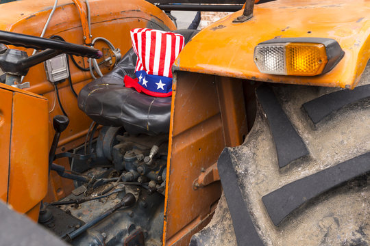 Close-up of an old rusty orange tractor with an american uncle sam hat with stars and stripes on the driver seat
