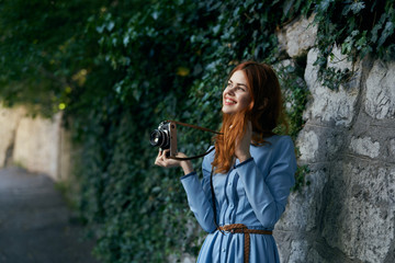 girl with a camera near a stone wall with leaves