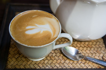 A cup of Latte art coffee on wooden plate with spoon and jug