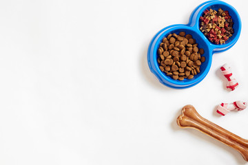 Dry pet food in bowl and bone on white background top view