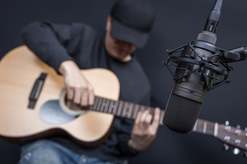 asian male musician recording acoustic guitar in sound studio