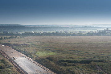 Unfinished asphalt country road. Under construction. Morning fog and sun