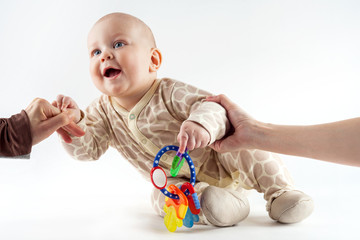 Parents' hands help baby to get up and take first step