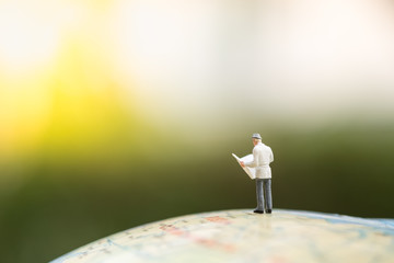 Business Concept. Businessman miniature figure standing and reading a newspaper on world balloon with green nature background