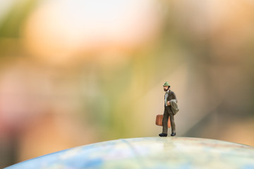 Business and travel concept. Businessman miniature figure with suitcase and jacket standing on...