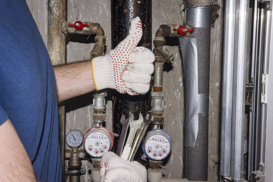 plumber with the wrenches in hands holds thumb up. Against backdrop of pipes and pressure gauges plumbing worker.