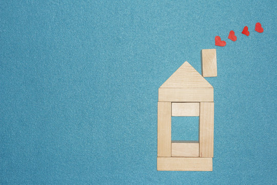 Love in home concept. Wooden house and red hearts from chimney pipe on blue background