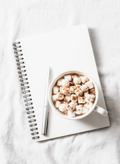 Hot chocolate with marshmallows and cinnamon, clean blank notepad on a light background. Christmas inspiration planning concept