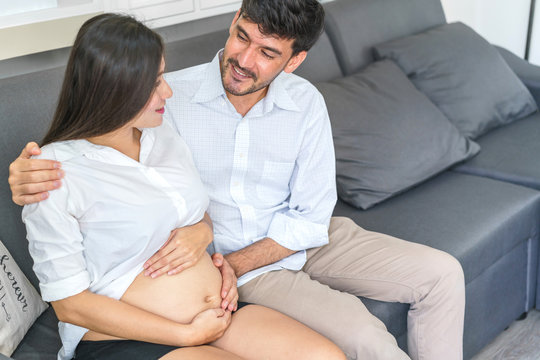 Handsome husband hugging beautiful pregnant woman and hands touch belly at living room. concept of pregnancy, family and lover relation.