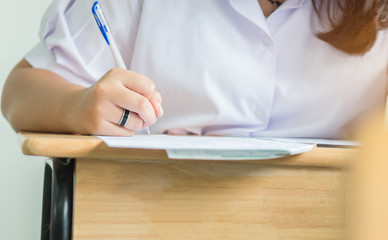 Girl Students holding pen taking exams, writing examination room with undergraduate students...