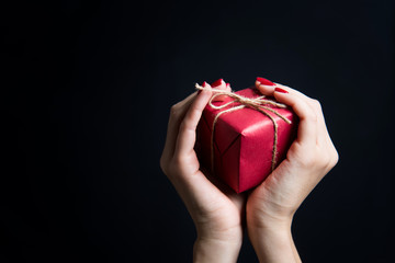 Young woman hands holding red gift box on black background