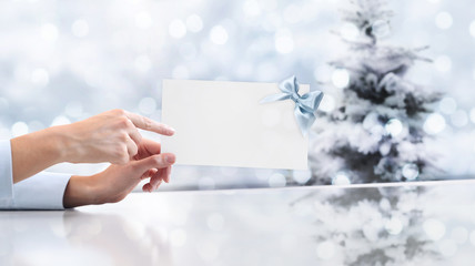 Obraz premium hand showing gift greeting card on christmas background with tree and blurred lights