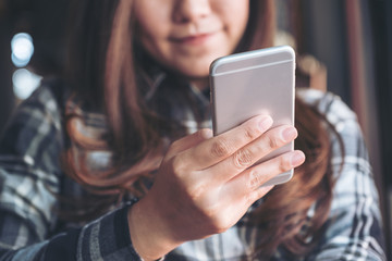 Closeup image of a beautiful Asian woman holding , using and looking at smart phone in modern cafe