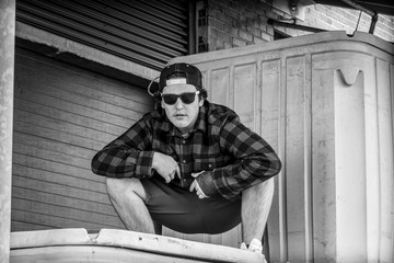 young man in plaid shirt and sunglasses in brick industrial alley in city